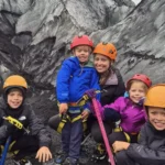 Family in helmets and harnesses posing with ice axes on a glacier in Iceland.