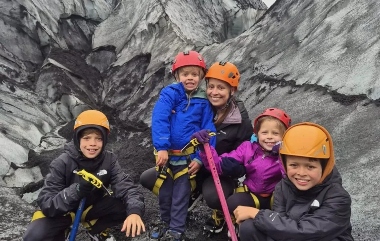 Family in helmets and harnesses posing with ice axes on a glacier in Iceland.