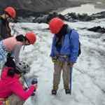 Glacier hikers in helmets adjust crampons and gear on an icy ridge.