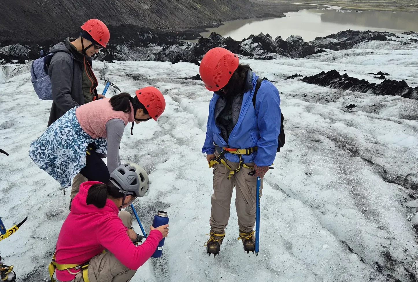 Glacier hikers in helmets adjust crampons and gear on an icy ridge.