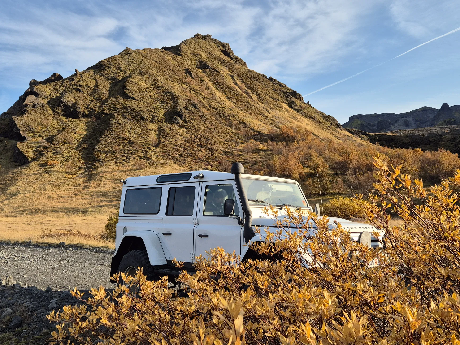 White 4x4 off-road vehicle in Iceland’s Thórsmörk Highlands with autumn shrubs and a mossy mountain backdrop.