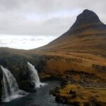Waterfall and stream beneath Kirkjufell mountain in Iceland under a cloudy sky.