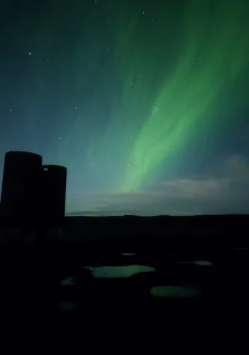 Green northern lights above a silhouetted building and dark landscape in Iceland.