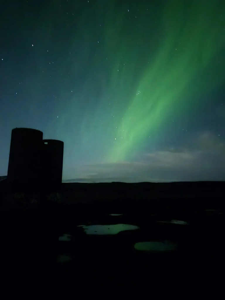 Green northern lights above a silhouetted building and dark landscape in Iceland.