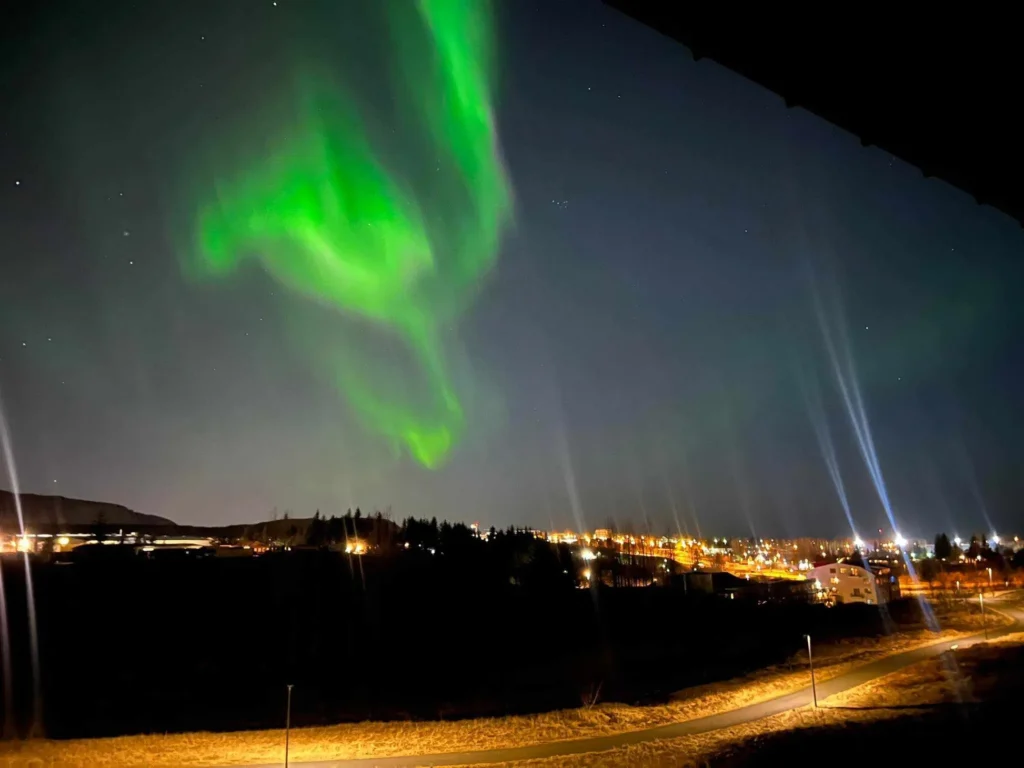 Green northern lights above a town’s glowing lights in Iceland.