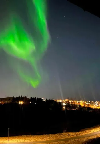 Green northern lights above a town’s glowing lights in Iceland.