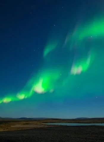 Green northern lights stretching across a dark Icelandic sky over open landscape.
