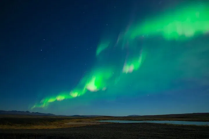 Green northern lights stretching across a dark Icelandic sky over open landscape.