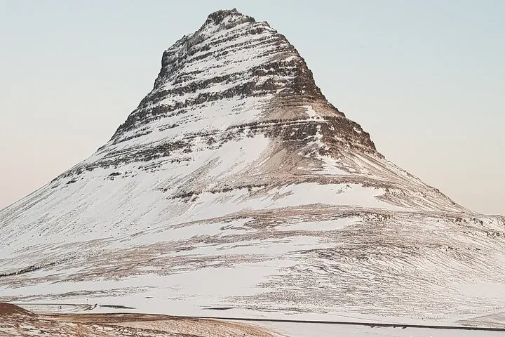 Snow-dusted Kirkjufell mountain on Icelands Snæfellsnes Peninsula, photographed against a pale sky.