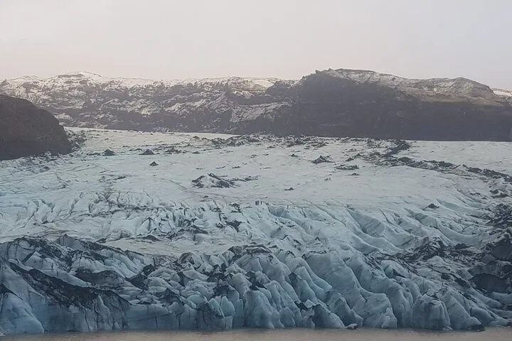 Vast Icelandic glacier with jagged blue ice stretching beneath snow-dusted mountains.