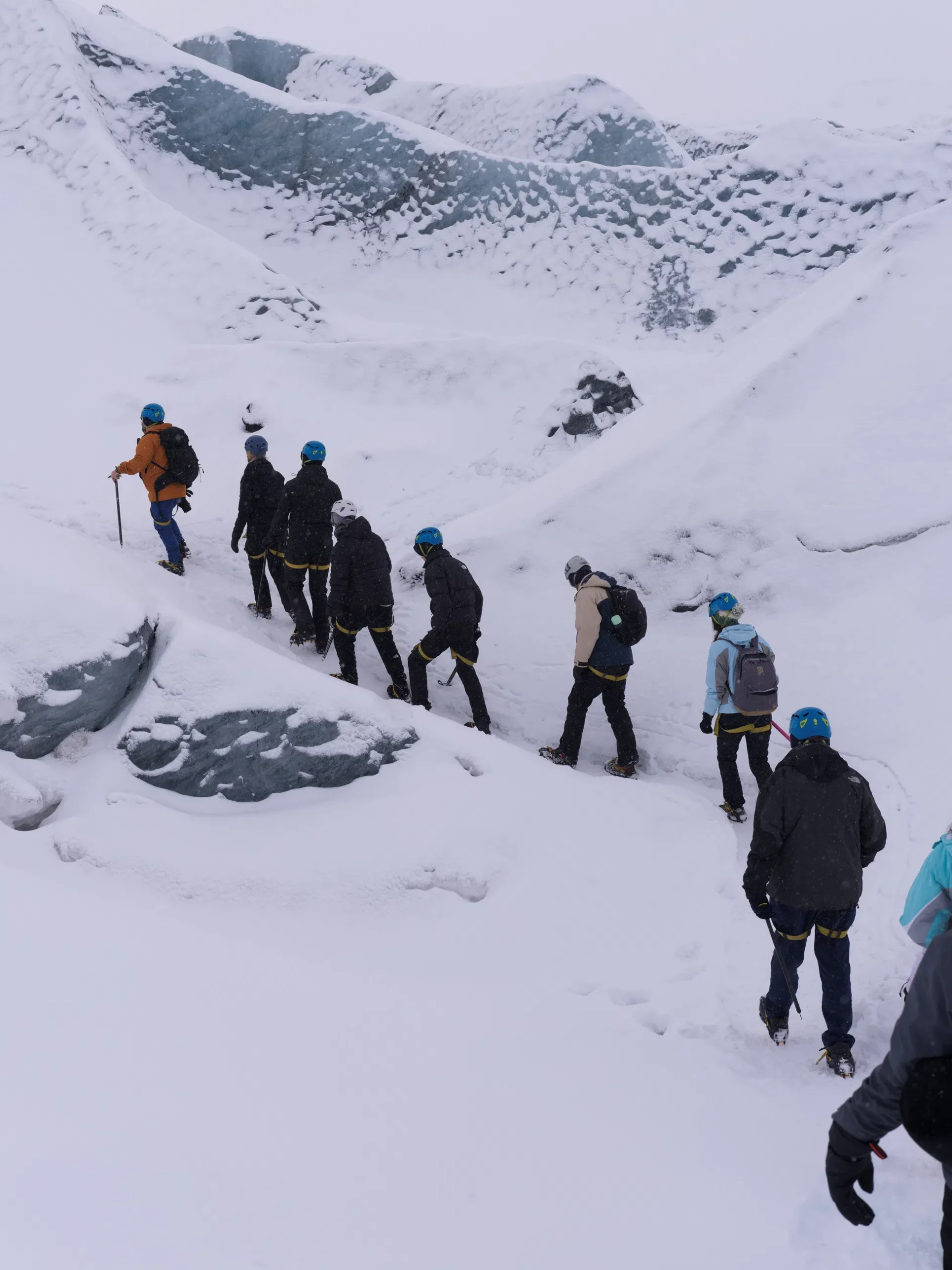 Glacier hikers in helmets adjust crampons and gear on an icy ridge.